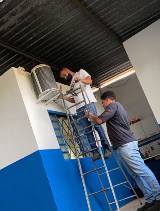 Dois técnicos em uma escada instalando a condensadora de um ar-condicionado em um comércio